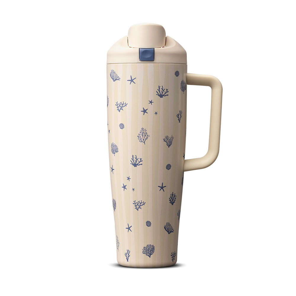 Owala Birthday Bash Coral Cabana 30oz FreeSip Tumbler; cream body with subtle vertical stripes scattered with small navy blue seashells, starfish, coral, and sea urchin illustrations, matching cream flip cap, lid, and side handle